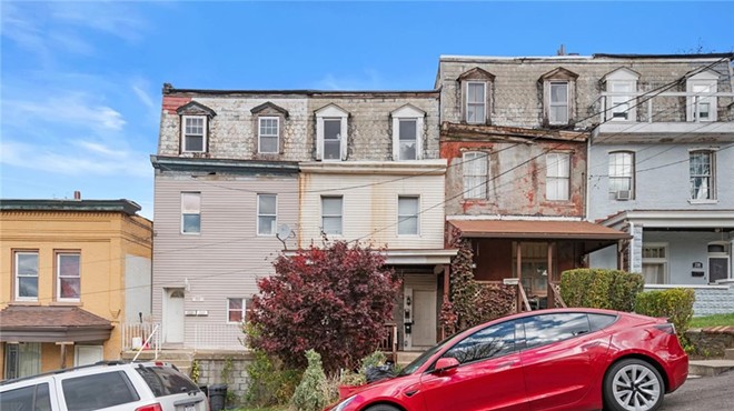 Tightly packed rowhouses with decayed façades on a steep street with parked cars.