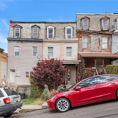 Tightly packed rowhouses with decayed façades on a steep street with parked cars.