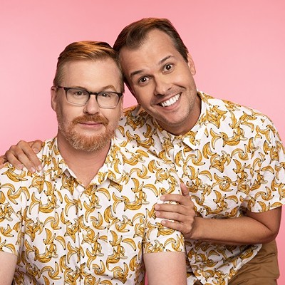 Two men wearing white button-down shirts featuring a banana print pose smiling in front of a pink background.
