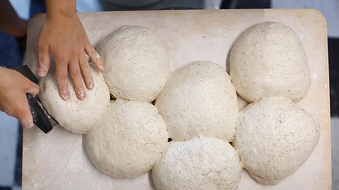A woman holds a tray of bread dough in a kitchen