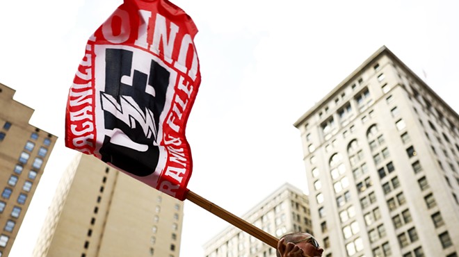 A person holds up a flag that says "organize" and "union" in front of tall city buildings