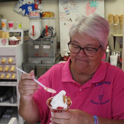 An older woman with short salt-and-pepper hair smiles in a pink shirt as she holds a large soft-serve parfait