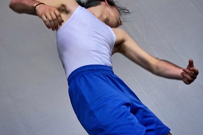 An artfully blurry shot of Pillow Project company dancer Theo Bliss in a white tank and blue shorts