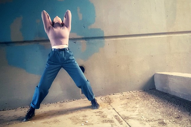 A dancer in a pink top and blue pants strikes a dramatic pose with her head thrown back.