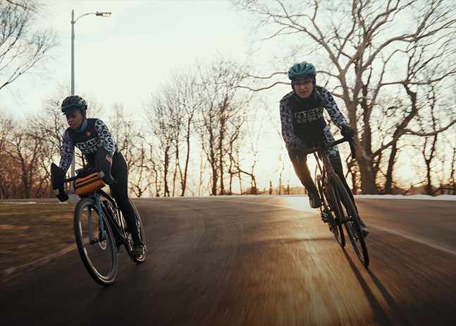 Two bicyclists round a corner, the sun at their backs.
