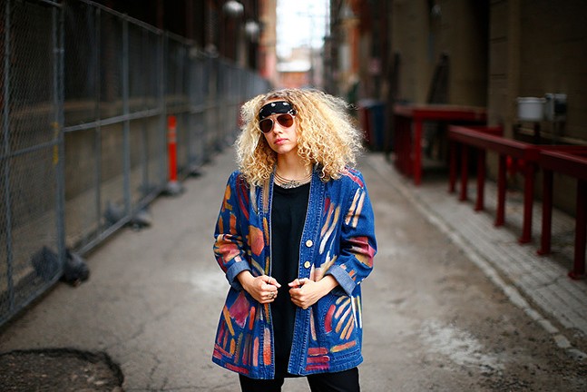 Musician Brittney Chantele stands wearing sunglasses and a multicolored jacket.