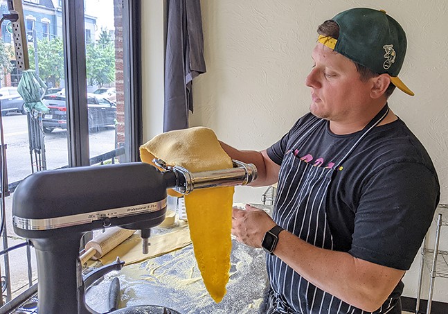 A man feeds dough through a pasta maker