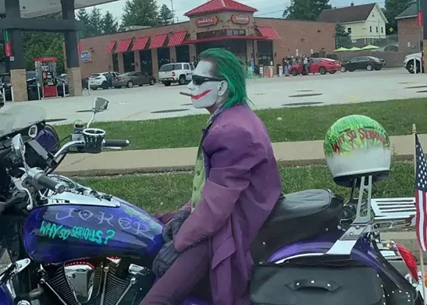 A guy dressed as the Joker, smoking a cigarette on a motorcycle that says "Why so serious?"