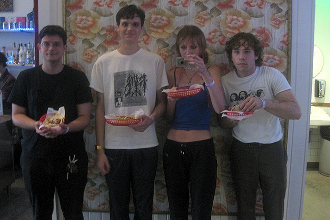 The band members of feeble little horse pose in front of colorful wallpaper while eating tacos