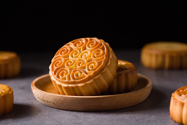 a mooncake, a round decorated pastry, in a wooden bowl surrounded by other mooncakes