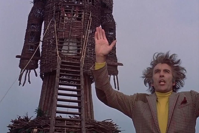 The late actor Christopher Lee stands dramatically in front of a giant wicker man in the film The Wicker Man.