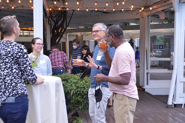 A group of people talk and drink on a patio decorated with string lights during Grow Pittsburgh's Garden Get Down event.