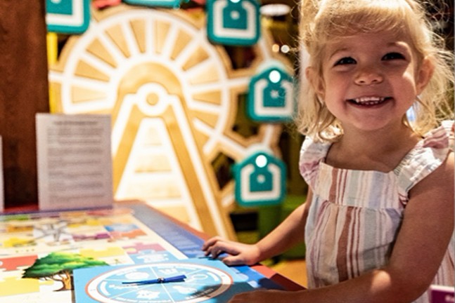 A little girl smiles at the camera as she interacts with an exhibit at Heinz History Center.
