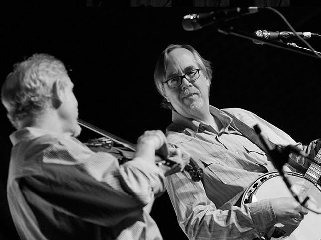 Two men playing string instruments in front of microphones