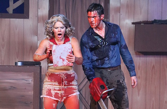 A blood-soaked couple stands on stage. The woman is screaming and the man is holding a chainsaw