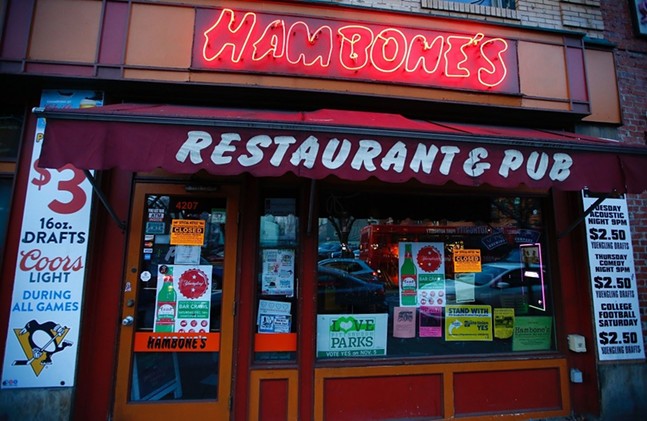 An exterior shot of a dive bar with a red neon sign reading "Hambone's" and a burgundy awning that reads "restaurant and pub."
