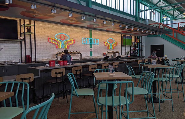 Wide shot of a brewery taproom awash in teal, pink, and yellow.