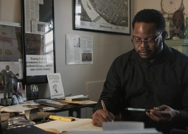 A Black man wearing glasses works at a desk.