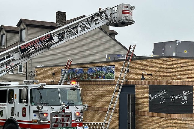 A red fire truck stretches its ladder over a one-story building.
