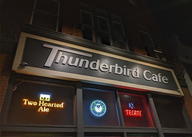 A sign for "Thunderbird Cafe and Music Hall" hangs over windows with neon beer signs in red, blue, and yellow.