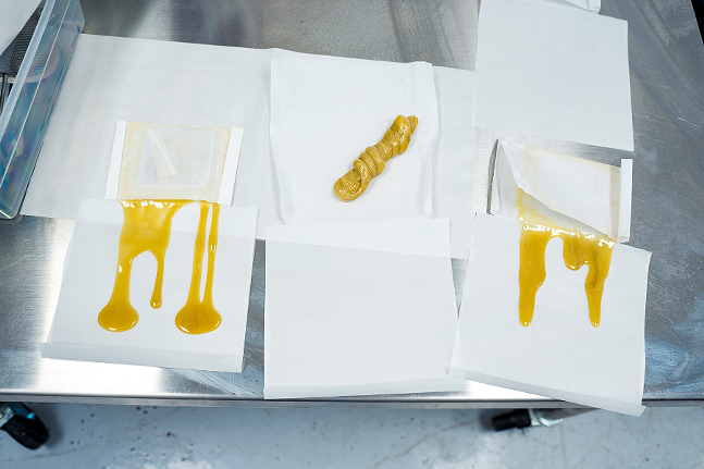 Image of live rosin in a lab setting on a metal table— yellow substance on white paper