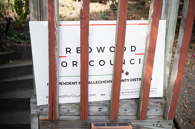 A Carl Redwood sign peeks from among wooden bars on a porch railing