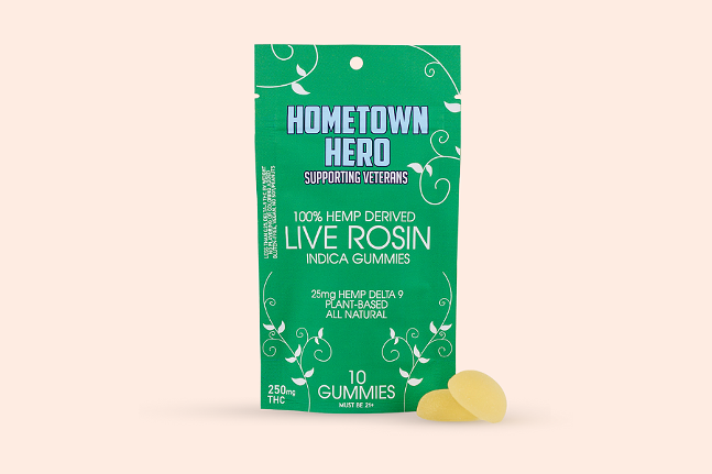 Pale pink background, image of green bag labeled "hometown hero supporting veterans 100% hemp derived live rosin indica gummies", with two yellow gummies placed in front of it