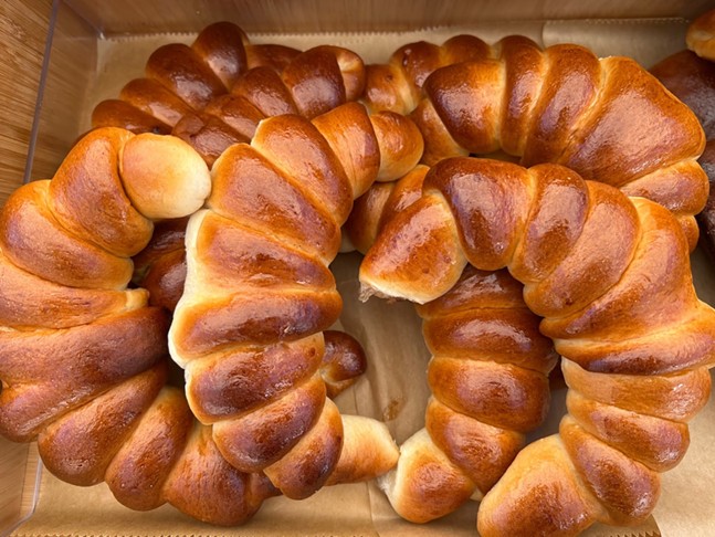 Golden brown, crescent-shaped yeast bread rolls are stacked on brown parchment paper.