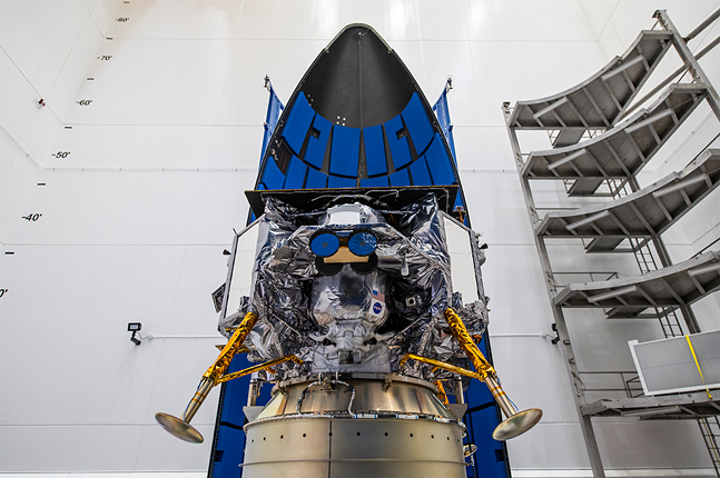 A shiny lunar lander is nestled in the padded nose cone of a rocket.