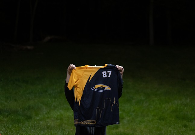 A person holds up a jersey with a gold sleeve, Thunderbird logo and black torso