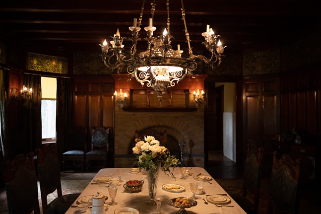 A chandelier hangs above a massive wooden table set with porcelain, silver and crystail