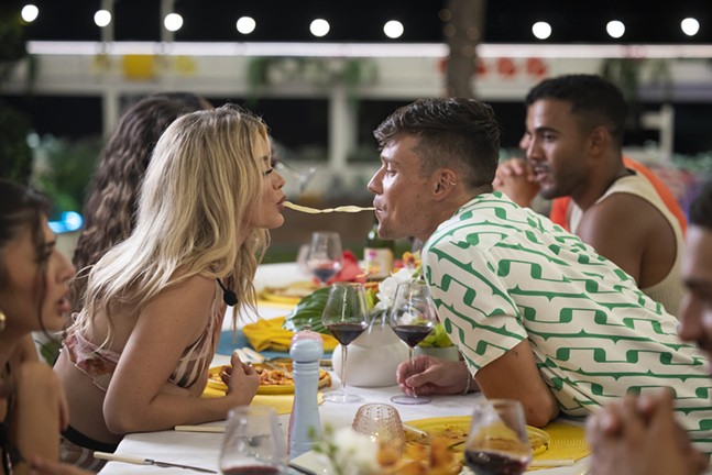 A young woman and man eat a spaghetti noodle from opposite ends