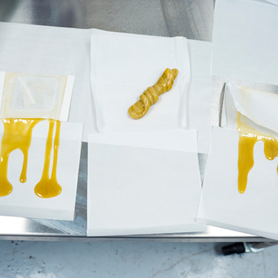 Image of live rosin in a lab setting on a metal table— yellow substance on white paper